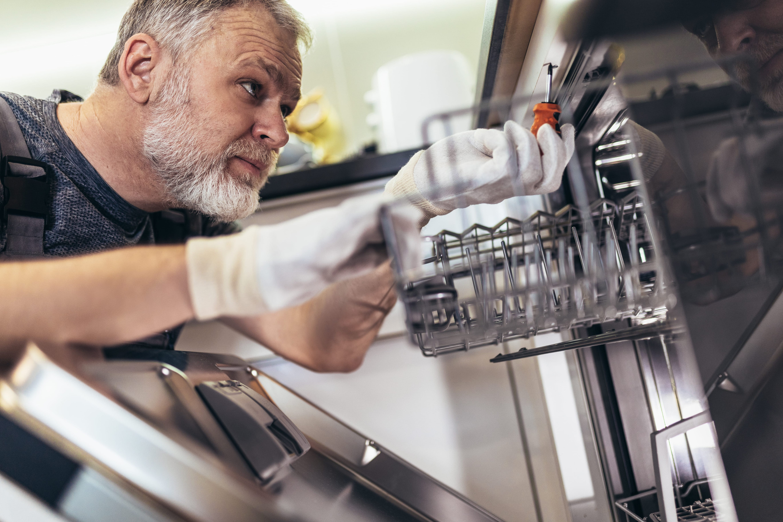 Man with toolbox repairing dishwasher in a household.