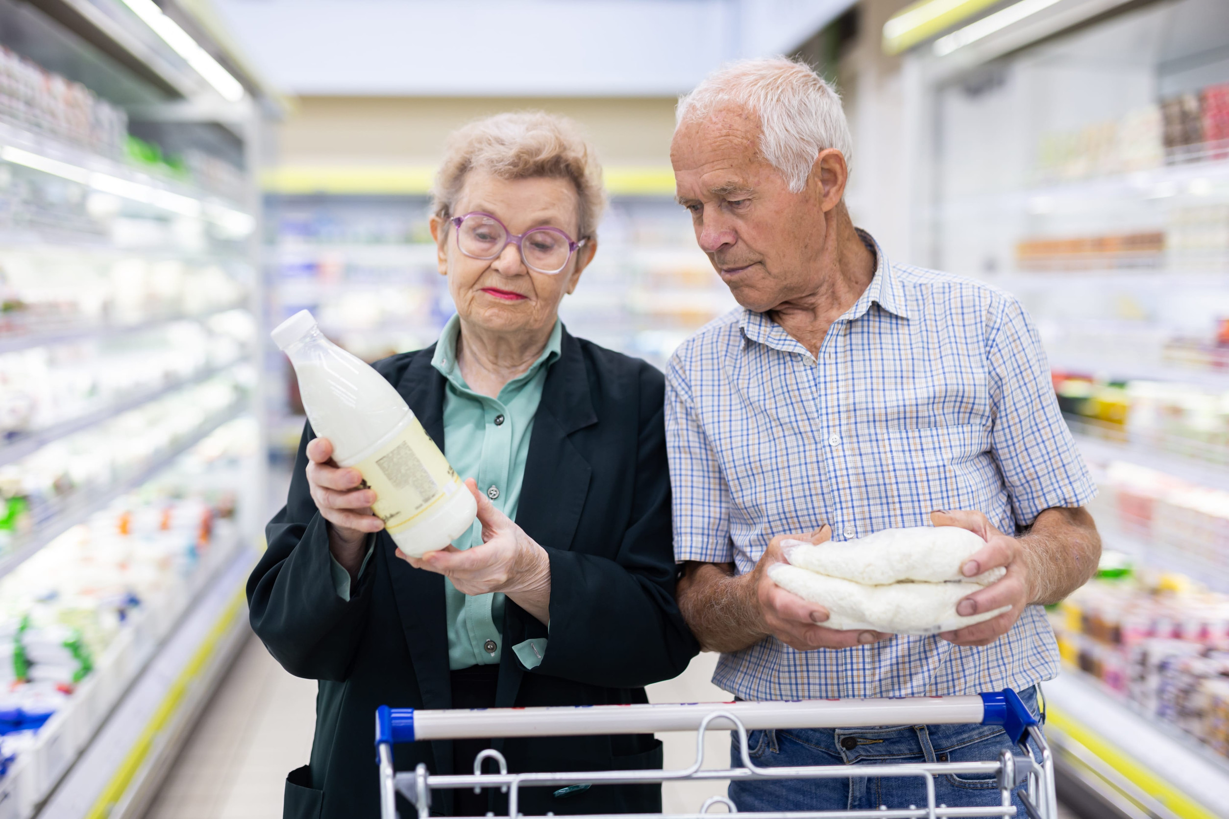 mature caucasian spouses chooses milk and cottage cheese in the dairy section of supermarket