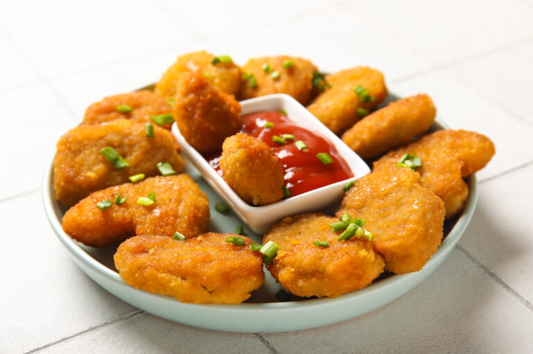 A delightful platter of crispy chicken nuggets, perfectly served with a side of tangy ketchup, garnished with fresh green onions for an added burst of flavor. Image Credit: serezniy/ 123RF
