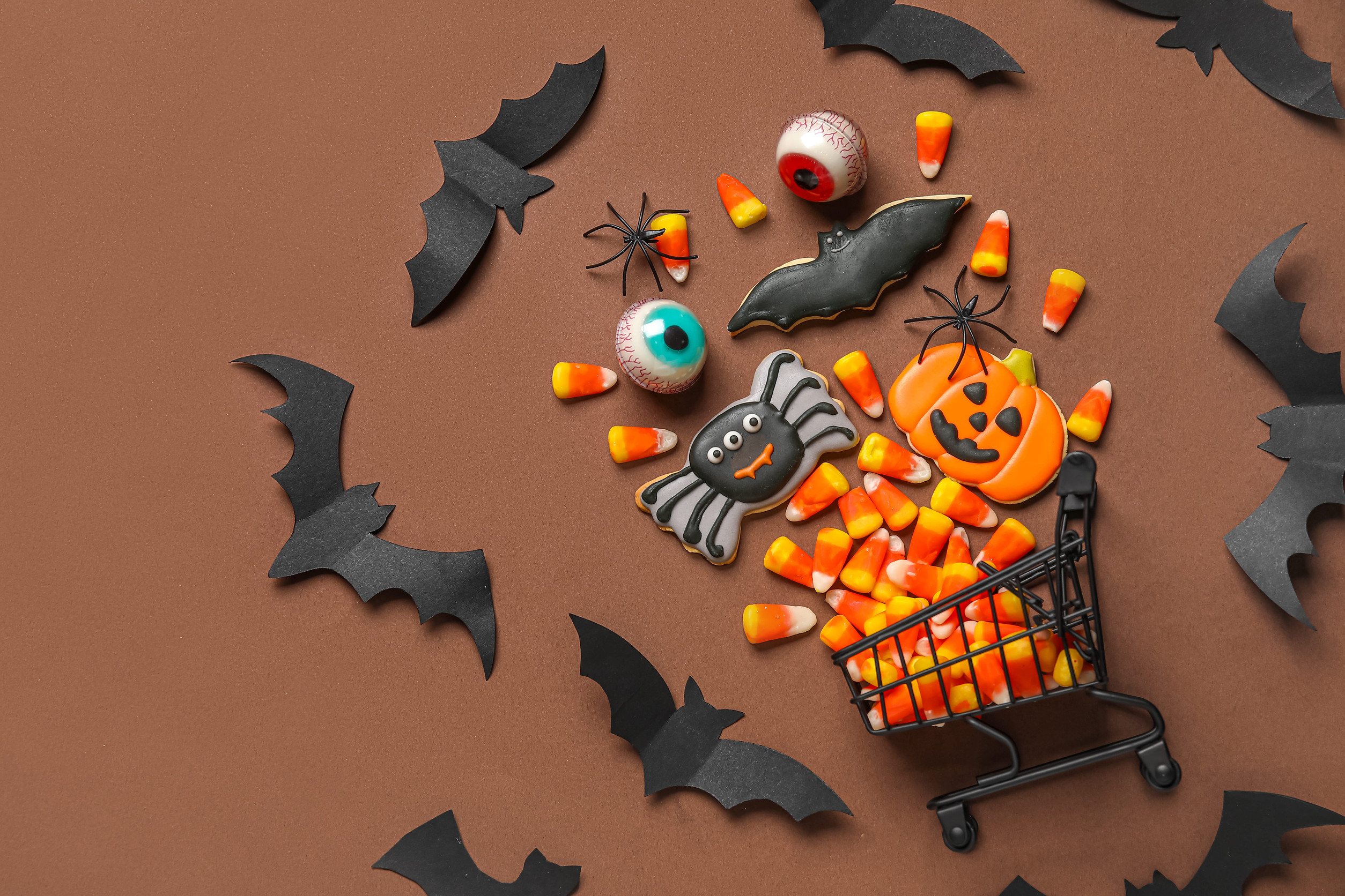 Shopping cart with tasty candy corns and cookies for Halloween on brown background