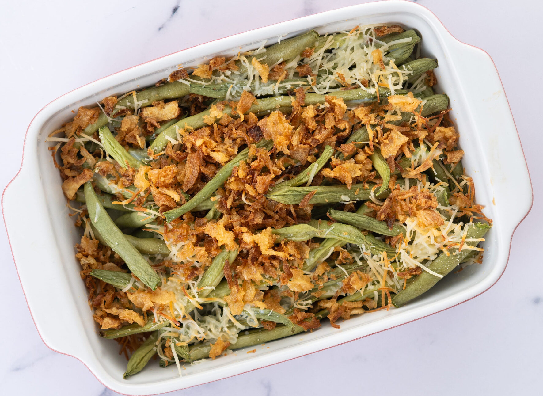 A traditional green bean casserole topped with French Fried Onions and cream of mushroom on white marble. close up