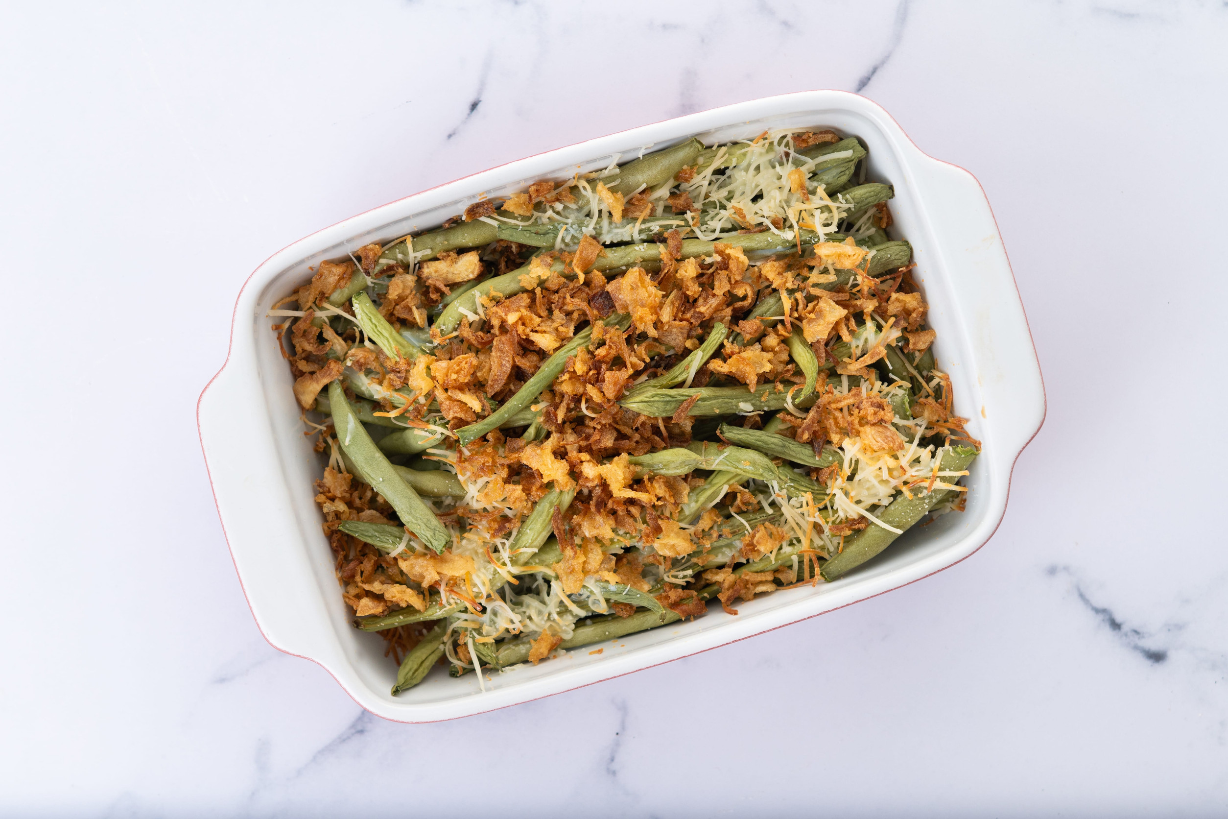 A traditional green bean casserole topped with French Fried Onions and cream of mushroom on white marble. close up