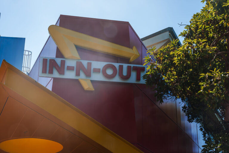 In N Out Burger iconic sign, red background, yellow arrow, building mount in San Francisco.