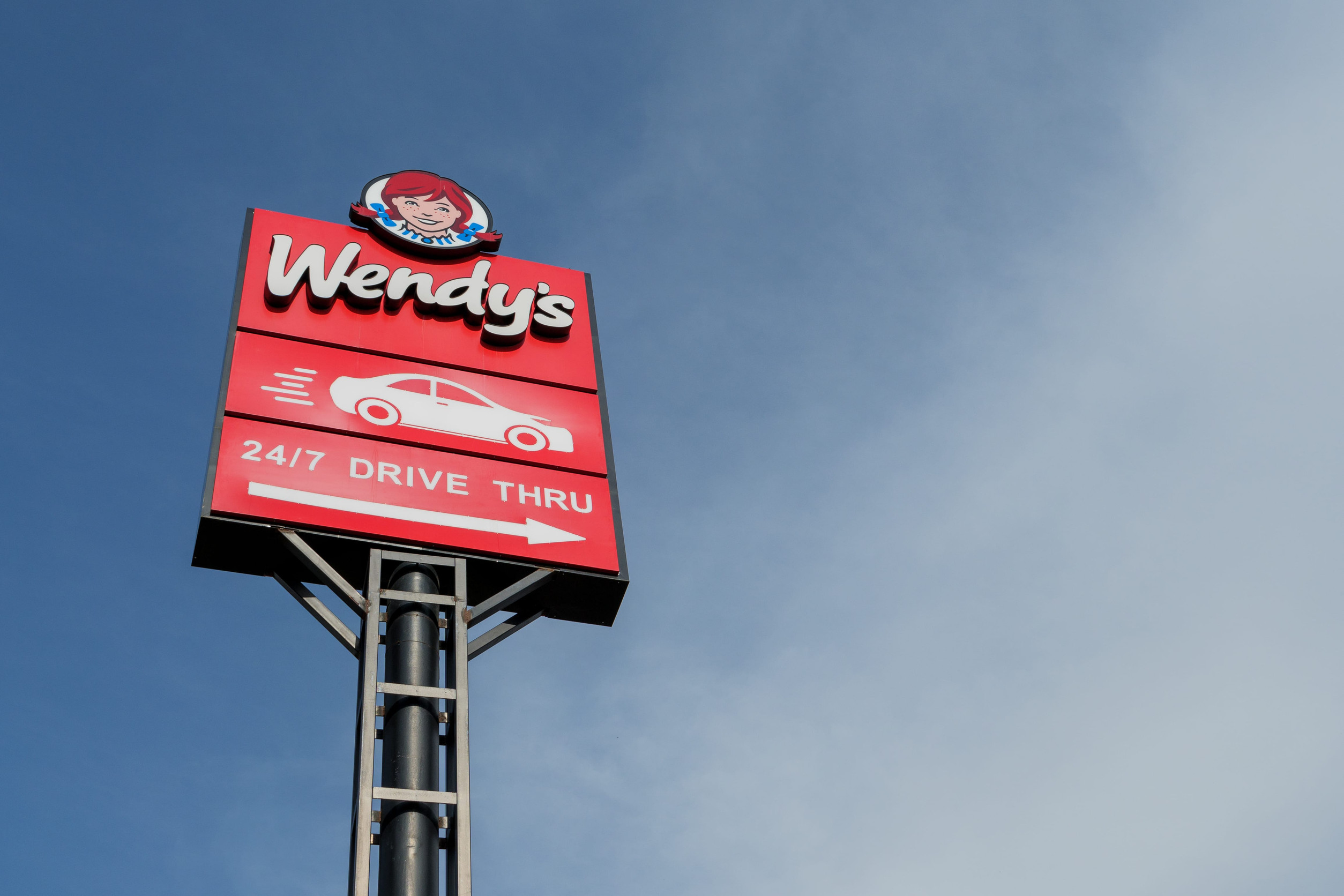 Wendys drive thru sign standing high against a blue sky background. Tbilisi, Georgia - June 17, 2024.
