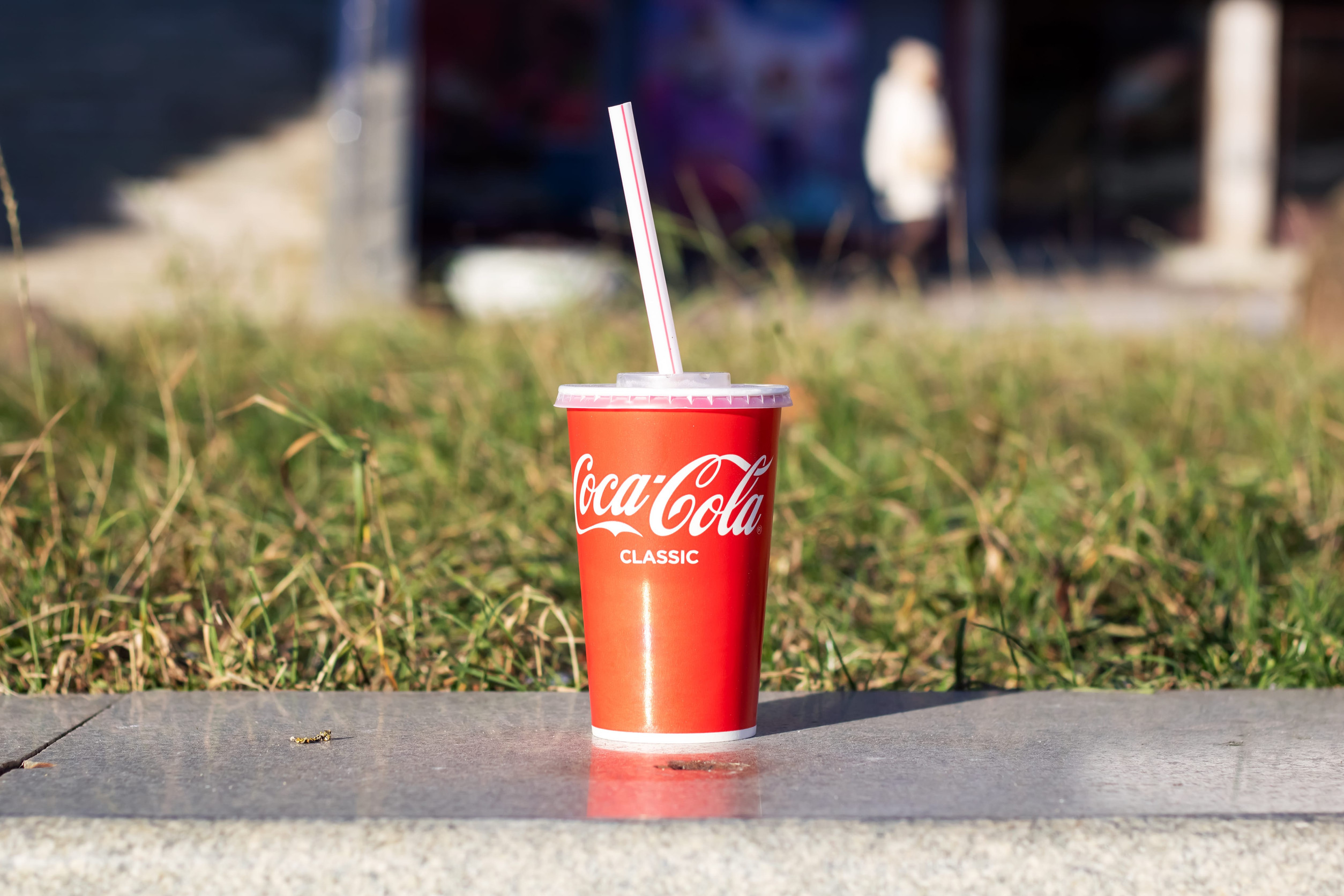 Belarus, Minsk - October 29, 2023: Glass of Coca Cola on curb by grass close up