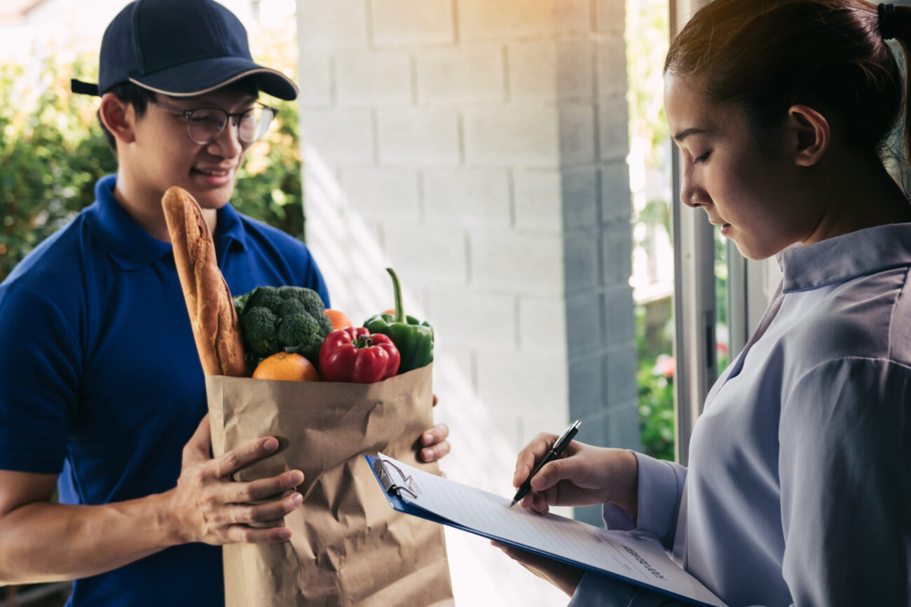 Asian woman is checking the product and signing the receipt on the order receipt through the online supermarket's home store. Image Credit: wutwhan/ 123RF