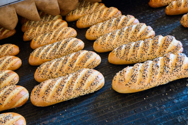 Freshly baked bread rolls with sesame seeds emerging from the oven at a bakery early in the morning. Image Credit: nordroden/ 123RF