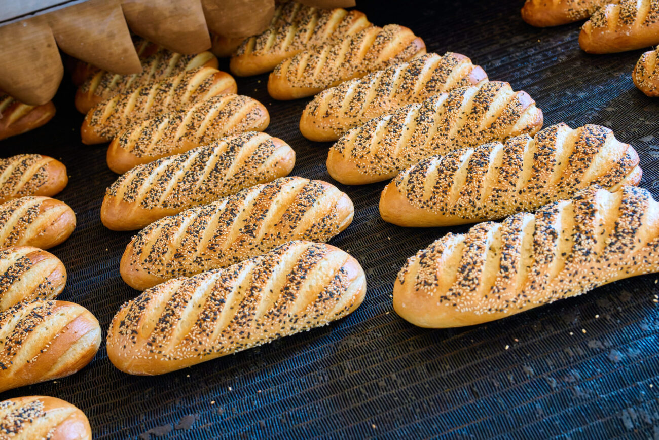 Freshly baked bread rolls with sesame seeds emerging from the oven at a bakery early in the morning. Image Credit: nordroden/ 123RF
