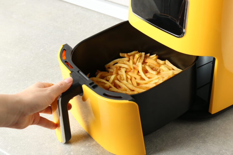 Woman cooking tasty French fries in air fryer at light gray table. Image Credit: liudmilachernetska/ 123RF