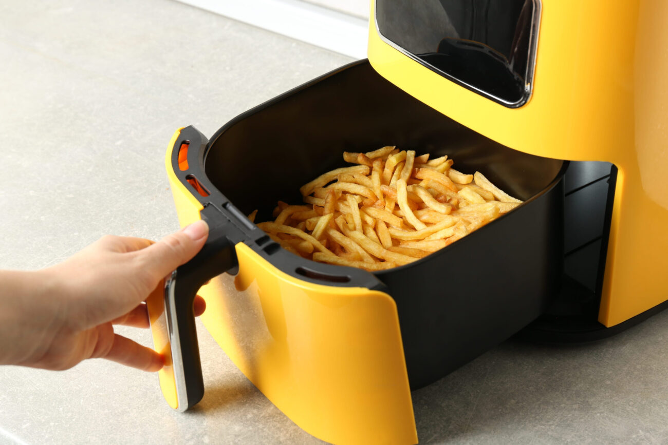 Woman cooking tasty French fries in air fryer at light gray table. Image Credit: liudmilachernetska/ 123RF