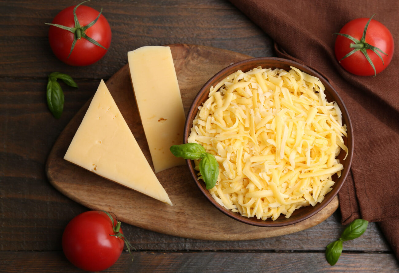 Grated and pieces of cheddar cheese with tomatoes on wooden table. Image Credit: liudmilachernetska/ 123RF