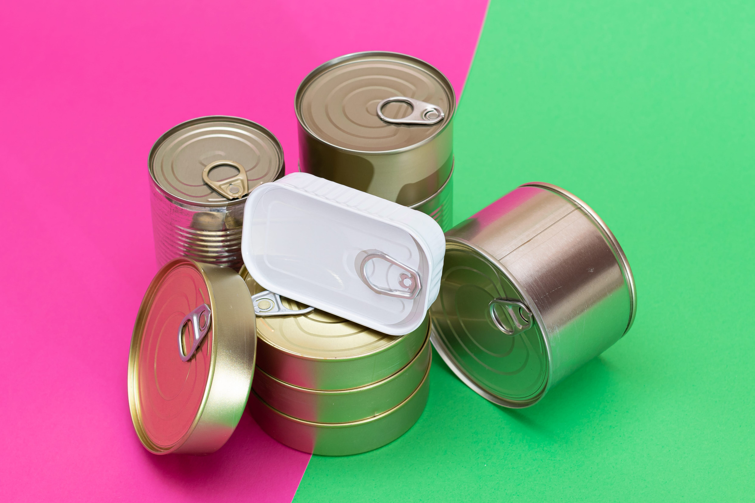 A Group of Stacked Tin Cans on Split Green and Cyan Background. Canned Food. Aluminum Cans for Safe and Long Term Storage of Food. Steel Sealed Food Storage Containers