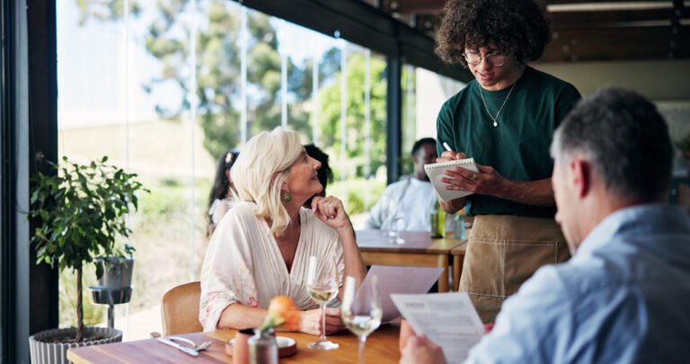 Woman, men and server with notes, service and talk for food with smile on date with partner at diner. Image Credit: peopleimages12/ 123RF