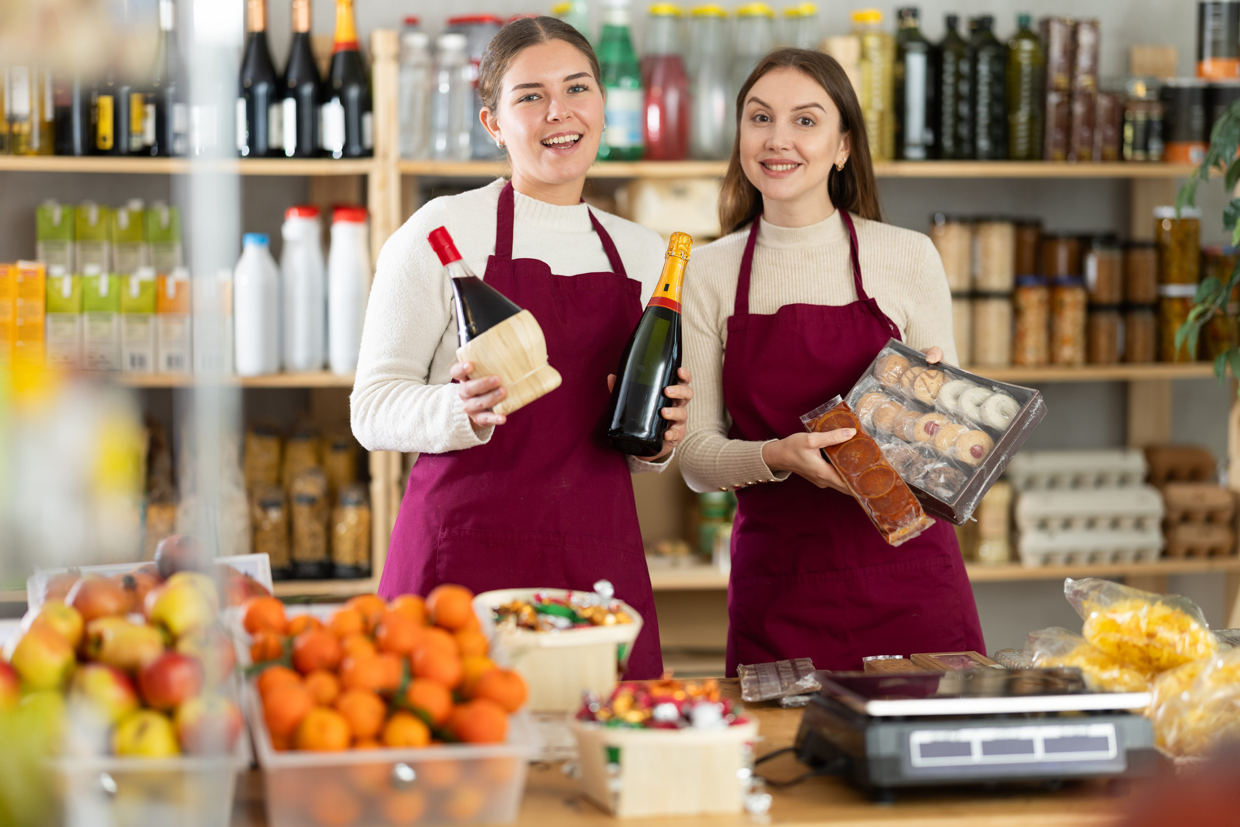 Young saleswomen are holding champagne, wine and sweets in their hands.
