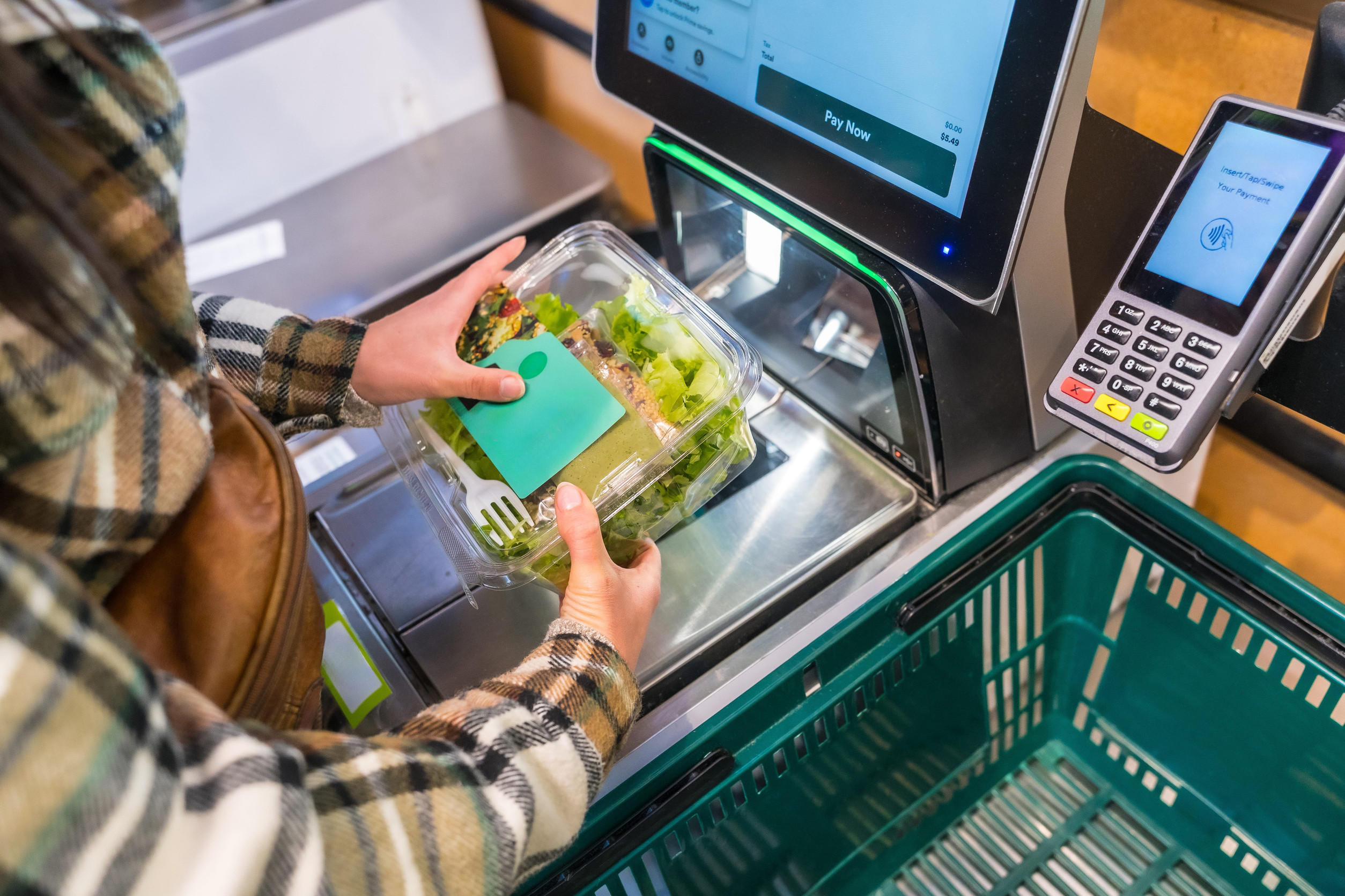 Woman using a self checkout machine, scanning a fresh salad in a plastic container at a grocery store, representing modern retail technology and shopping convenience