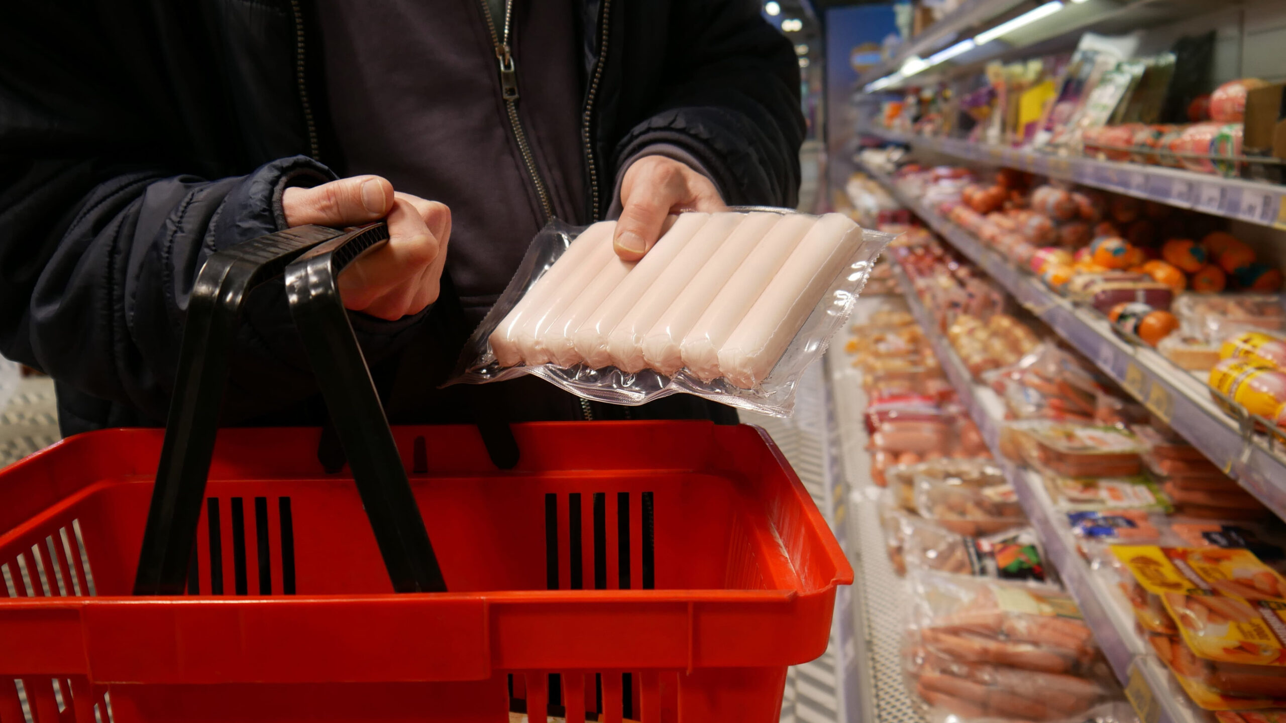 Close-up of a customer's hands putting a package of sausages into a shopping basket