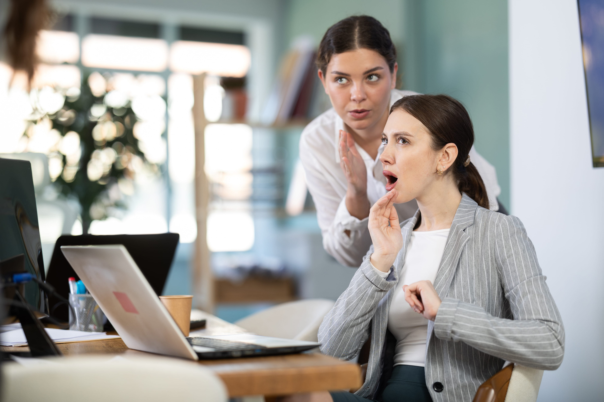 Female employee sharing gossip with surprised young colleague