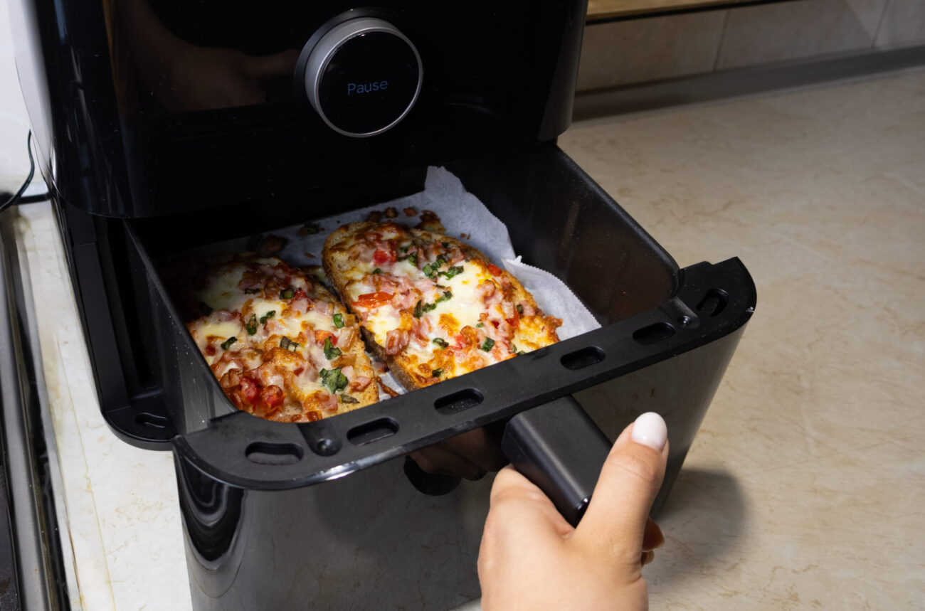 Woman taking slices of pizza out of an air fryer in the kitchen. Image Credit: iulia01/ 123RF