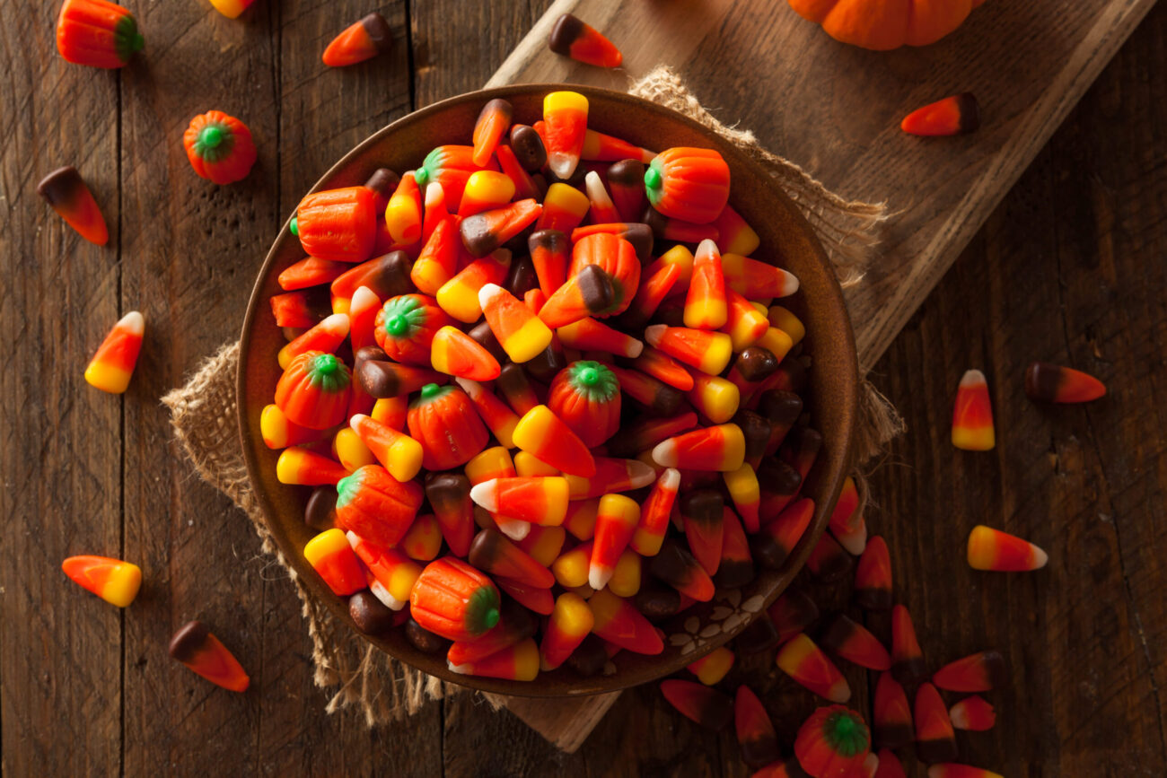 A festive autumn display showcases a bountiful bowl brimming with colorful candy corn and vibrant pumpkin-shaped sweets, capturing the spirit of Halloween and the joy of seasonal treats. Image Credit: bhofack2/ 123RF