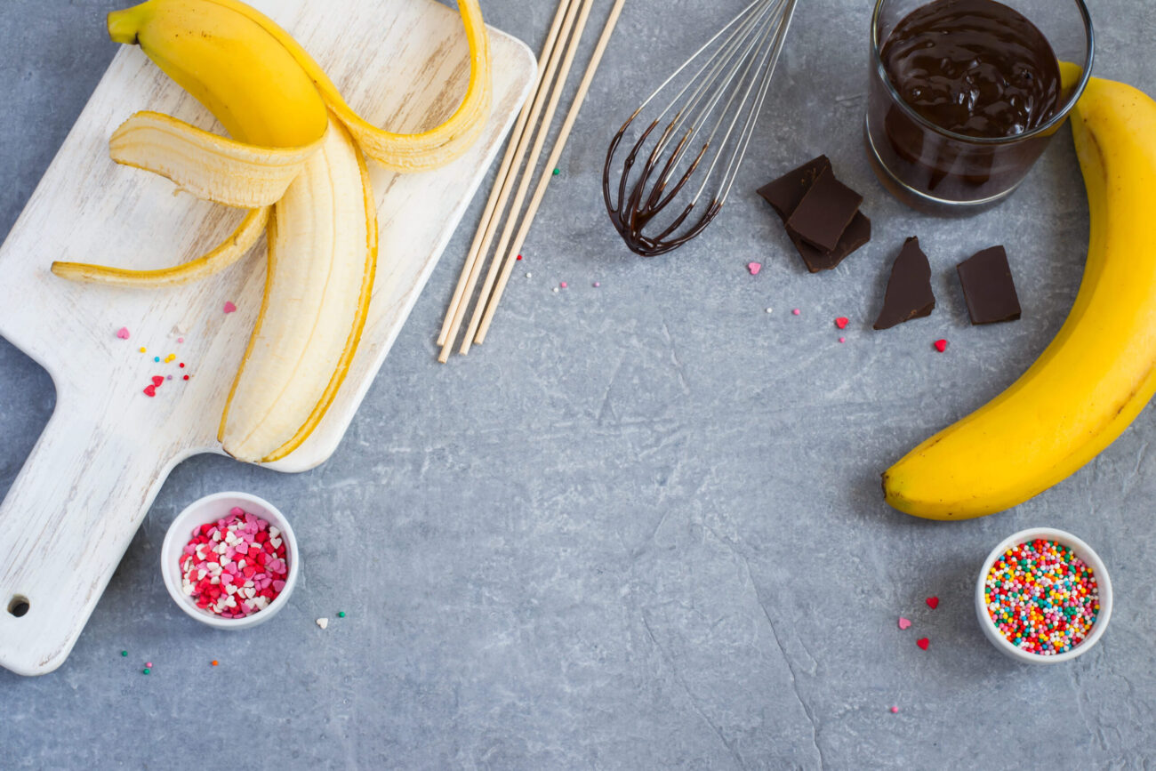 bananas, dark chocolate, sweet sprinkling and cutting board, gray concrete background. Image Credit: colnihko/ 123RF
