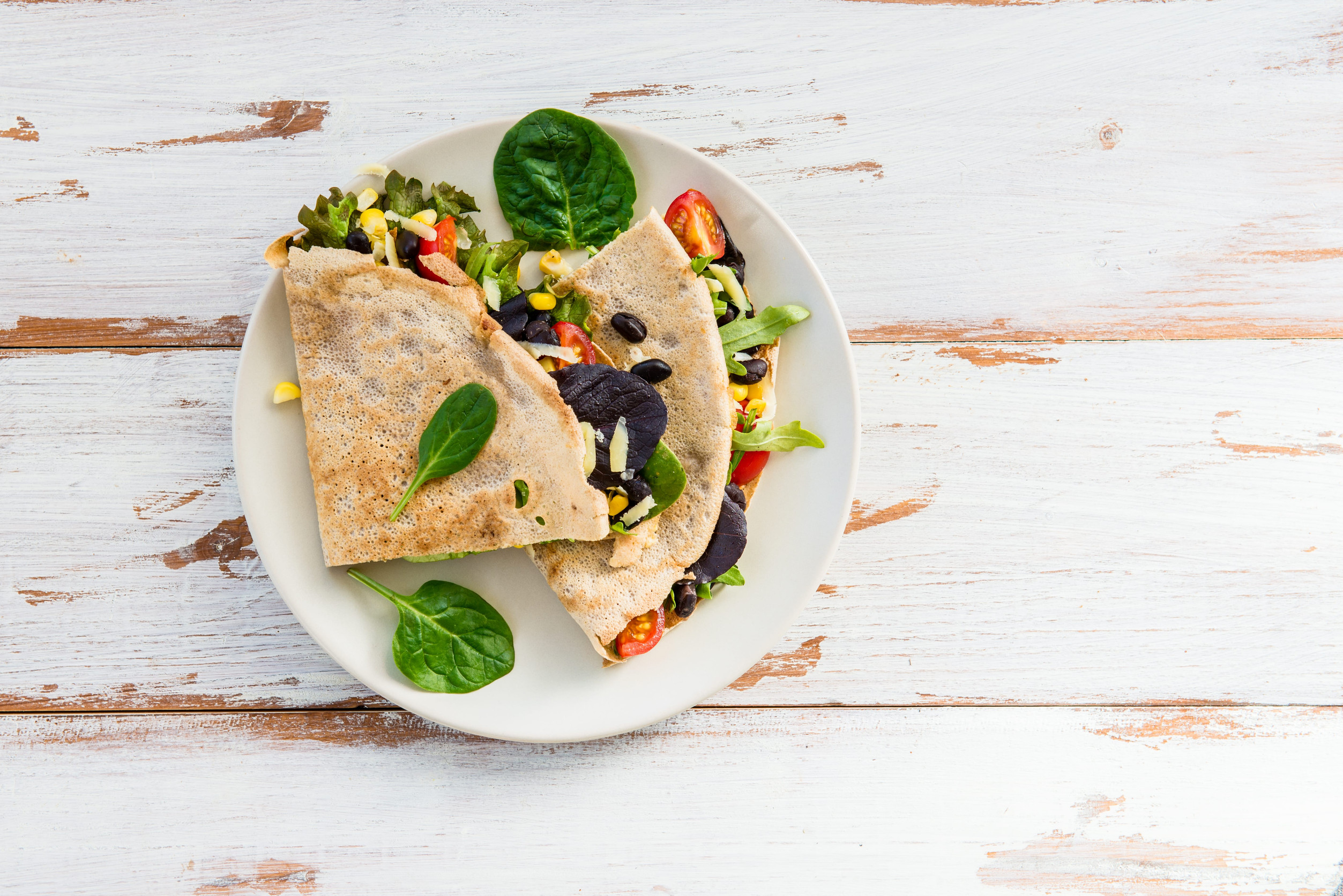 Healthy Warm Snack from Savoury Buckwheat Pancake or Quesadilla with Black Beans, Corn, Cherry Tomatoes, Rocket Salad, Spinach, Cheddar Cheese on White Wooden Background