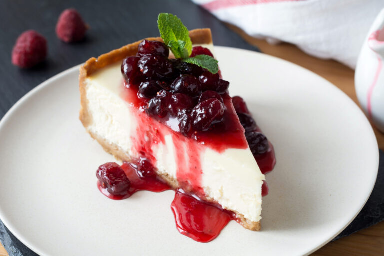 Slice of cheesecake with cranberry sauce decorated with mint on white plate. Image Credit: arx0nt/ 123RF