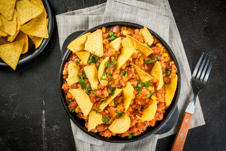Traditional Mexican Chilean food, chili con carne, served in a portioned skillet pan with nachos tortilla. On black concrete table, top view copy space