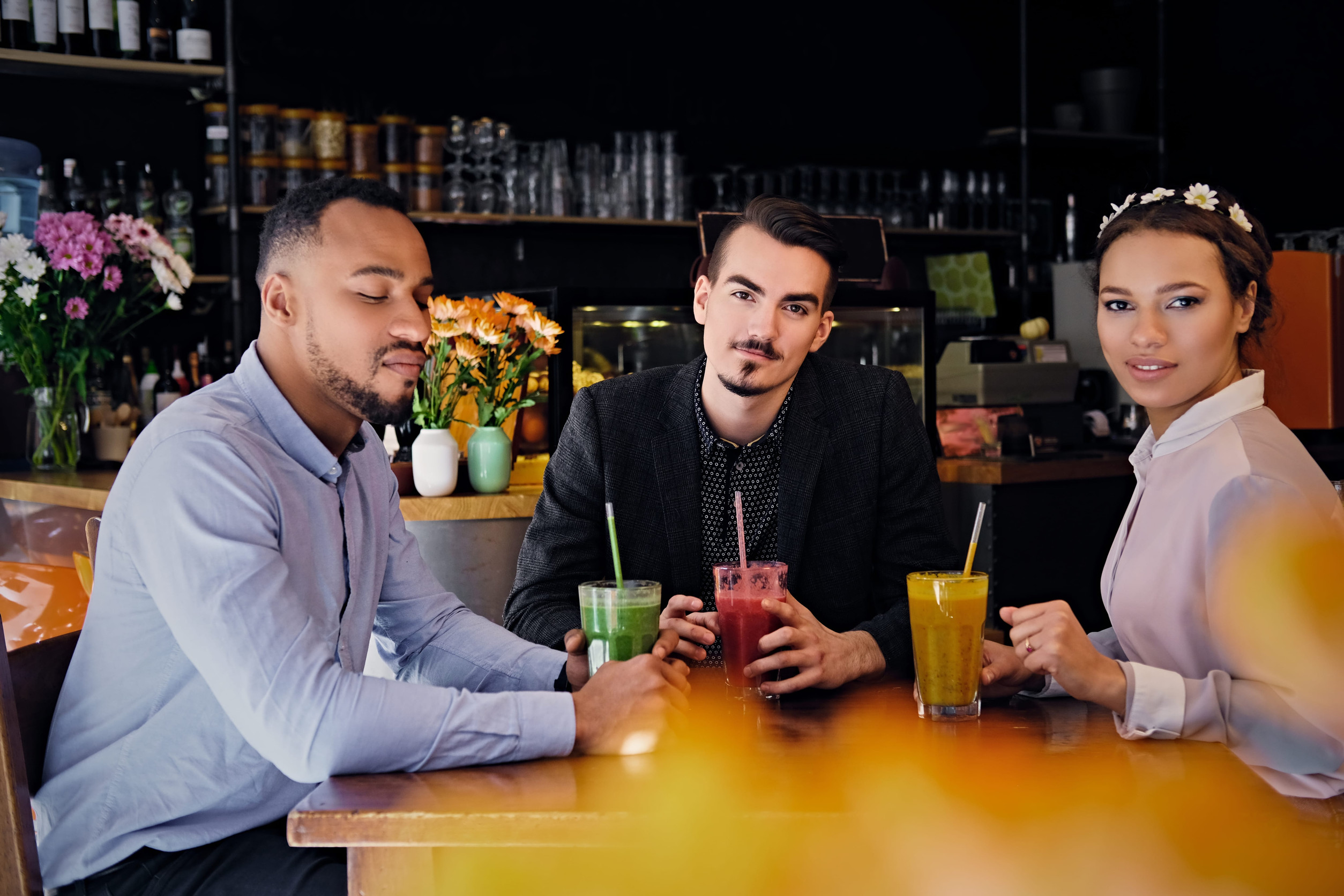 Three multiracial friends drink refreshing vegetarian juice cocktails in a cafe.