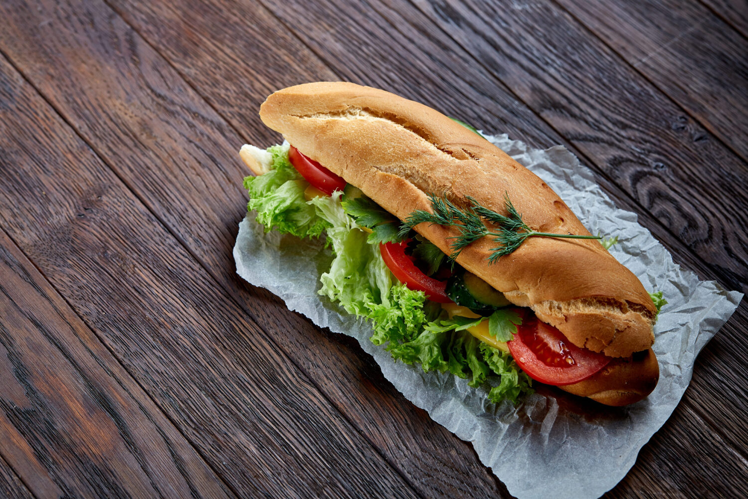 A delicious sandwich stacked high with fresh lettuce, ripe tomatoes, and crisp cucumbers, resting on a rustic wooden table. Perfect for a quick lunch or a satisfying snack, this culinary delight is as pleasing to the eye as it is to the palate. Image Credit: alekseyrezin/ 123RF
