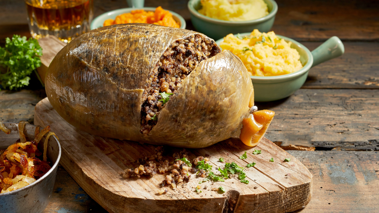 A traditional Scottish feast takes center stage, featuring a beautifully presented haggis, surrounded by a variety of comforting sides. The rustic wooden table offers an inviting atmosphere, perfect for sharing stories and toasting to good health with a glass of whisky. Image Credit: foodandmore/ 123RF