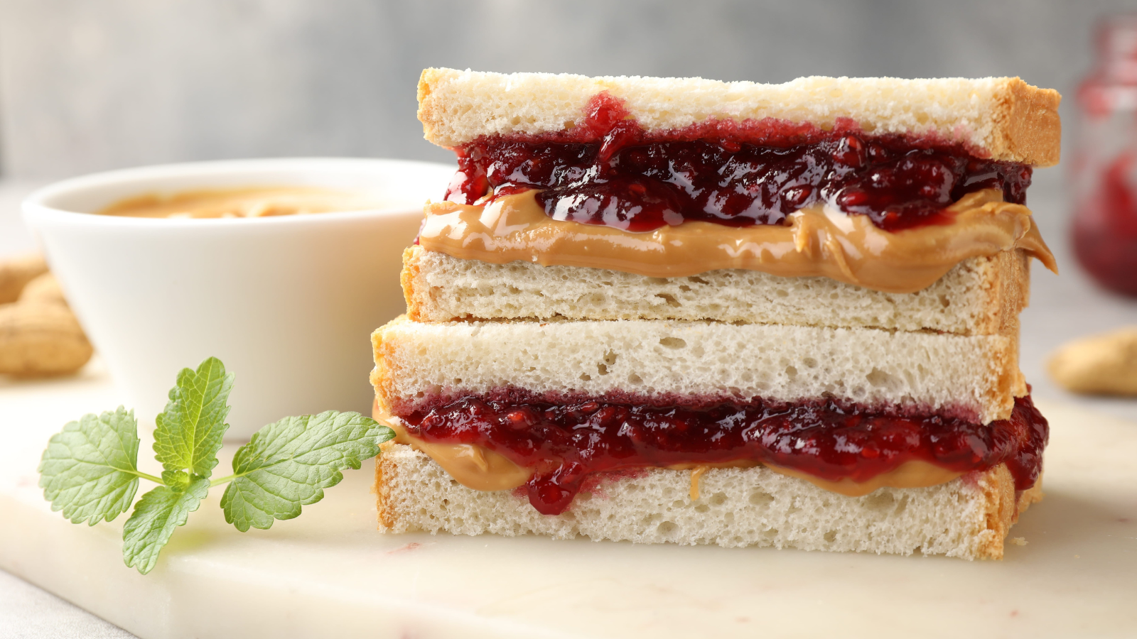 Tasty sandwiches with peanut butter, jam, nuts and mint on grey table. Image Credit: liudmilachernetska/ 123RF
