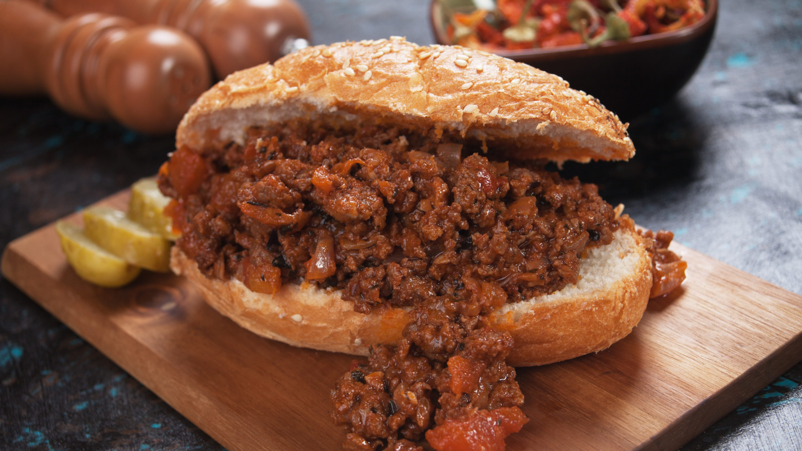 A hearty and flavorful sloppy joe, served on a fresh bun, oozing with rich beef and tangy sauce, perfectly complemented by a side of pickles and a colorful salad in the background. This classic comfort food embodies the essence of indulgence, making it a delightful treat for any meal. Image Credit: igordutina/ 123RF
