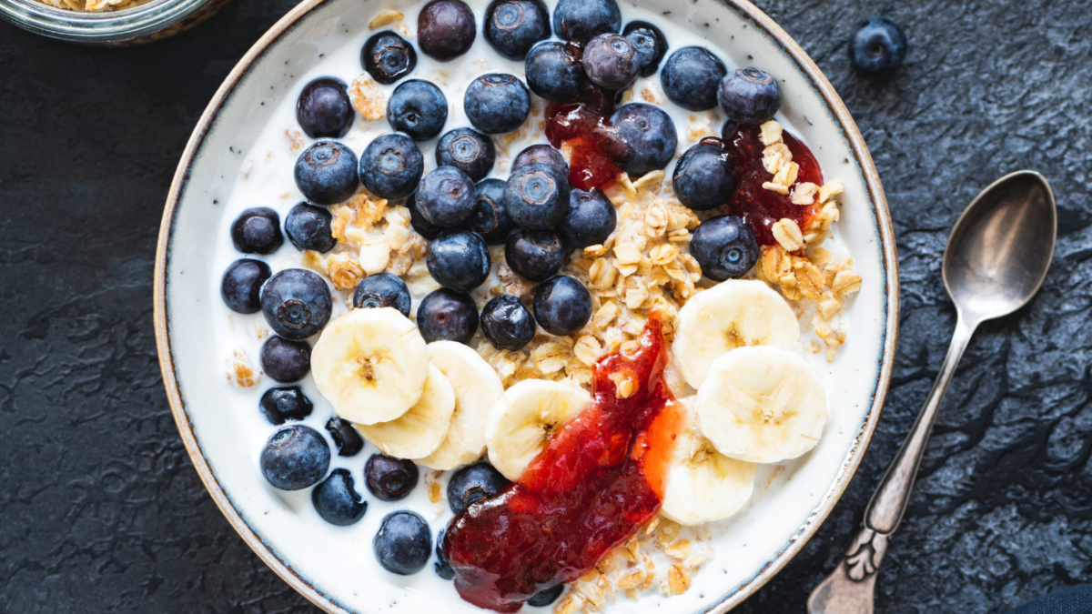 A delightful bowl of yogurt topped with fresh blueberries, sliced bananas, and a drizzle of berry jam, accompanied by crunchy granola and ripe bananas, making for a perfect breakfast scene. Image Credit: arx0nt/ 123RF