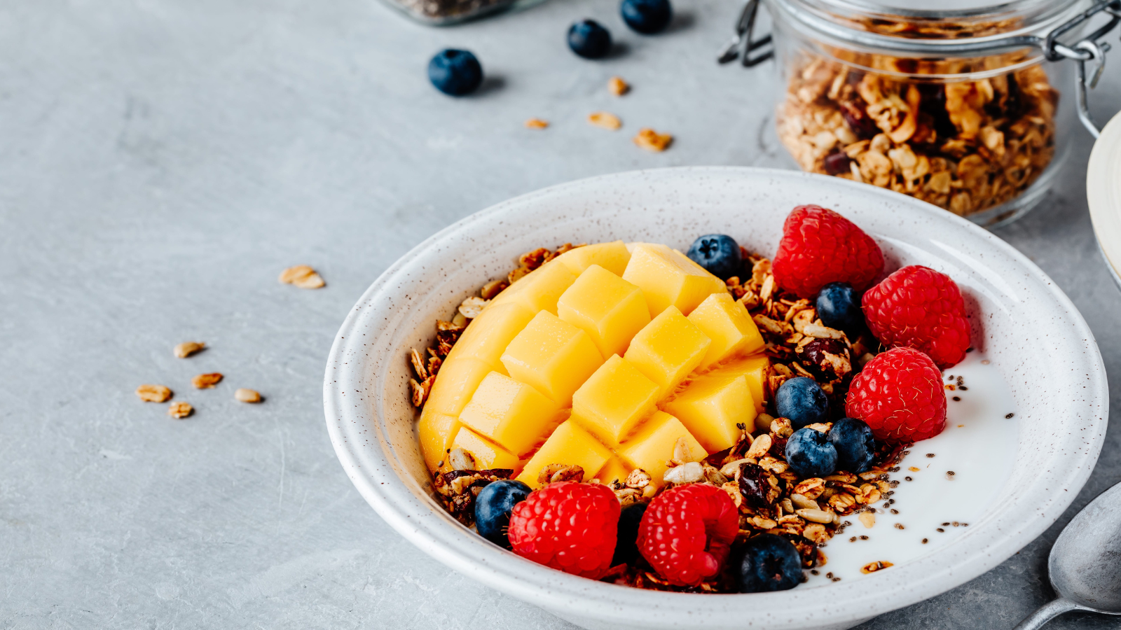 A vibrant breakfast bowl showcasing fresh mango, luscious raspberries, and blueberries nestled on a bed of crunchy granola, perfect for a healthy start to the day. Image Credit: nblxer/ 123RF