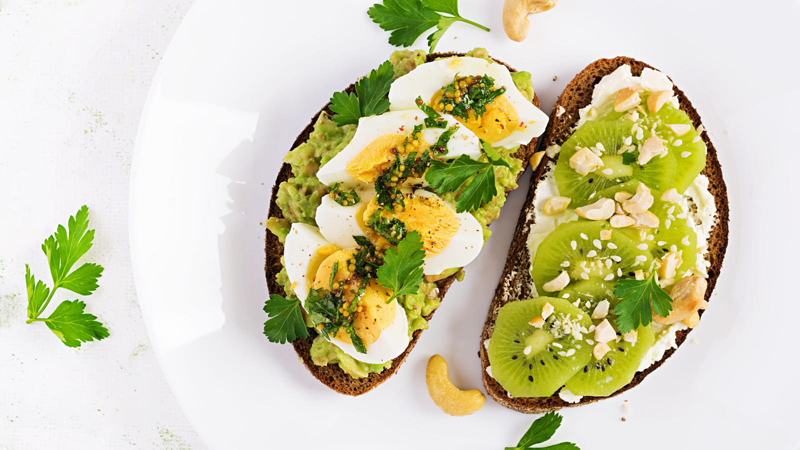 A delightful brunch plate featuring creamy avocado toast topped with perfectly sliced eggs and a refreshing kiwifruit spread on whole grain bread, garnished with fresh herbs and nuts for a burst of flavor. Image Credit: timolina/ 123RF