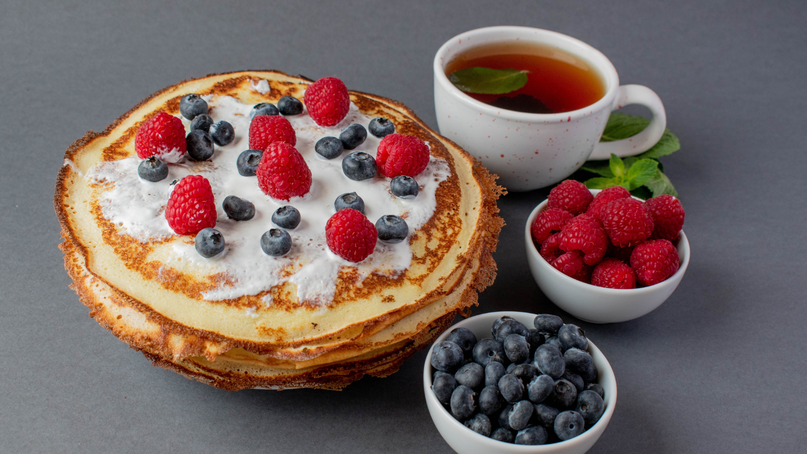 Indulge in a delightful brunch featuring fluffy pancakes adorned with fresh raspberries and blueberries, complemented by a steaming cup of herbal tea. Perfect for a cozy morning treat. Image Credit: kyralutsenko/ 123RF