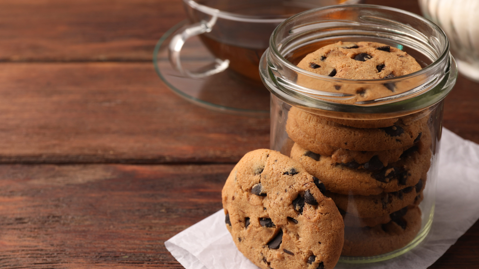 Glass jar with delicious chocolate chip cookies and tea on wooden table. Image Credit: liudmilachernetska/ 123RF