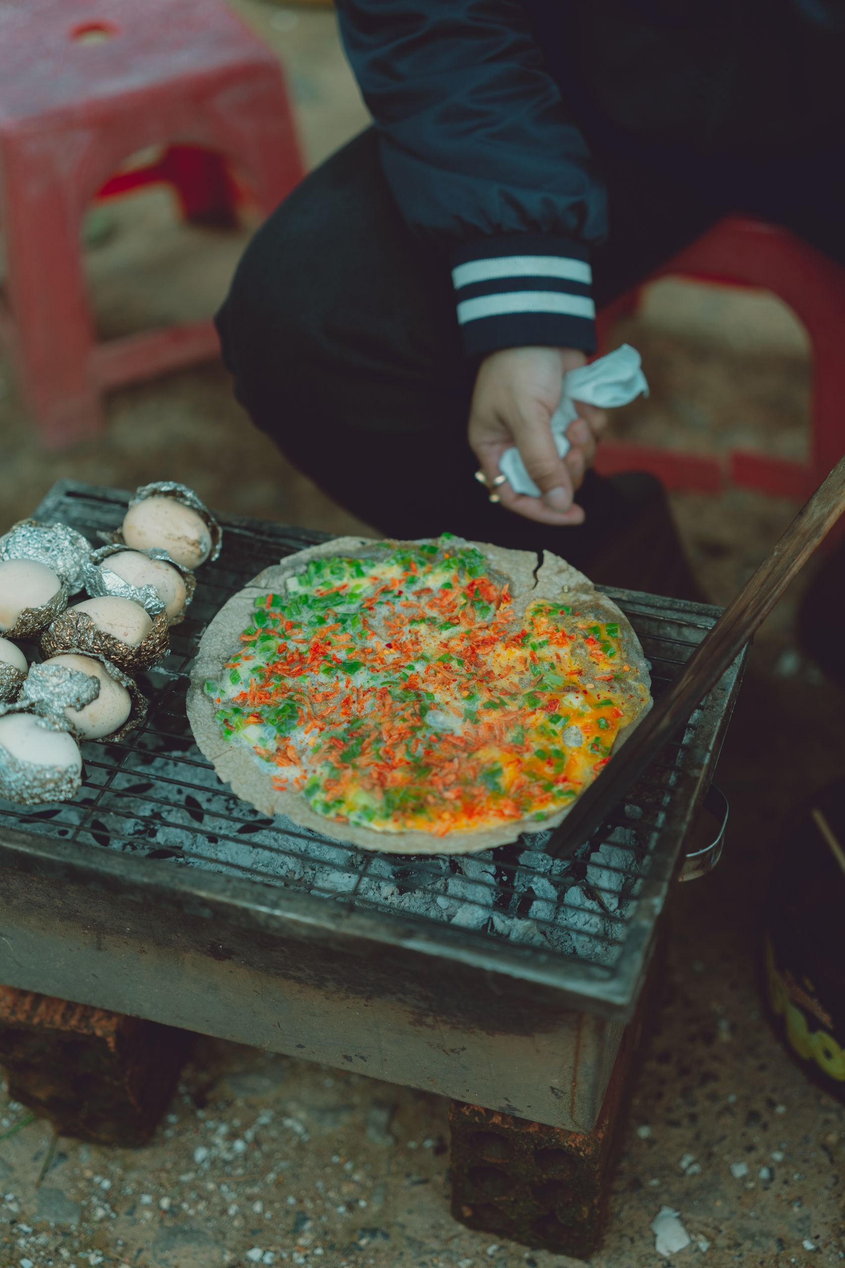 A close-up of a colorful rice pancake grilling on charcoal in Dalat, Vietnam street setting.