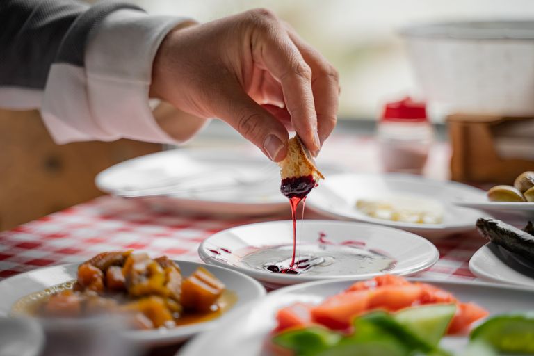 A close-up of a hand dipping bread in jam during a cozy breakfast in Bursa, T&uuml;rkiye.