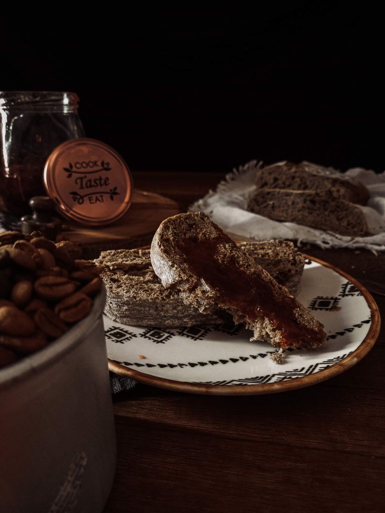 A close-up of rustic bread with jam and coffee beans on a wooden table.