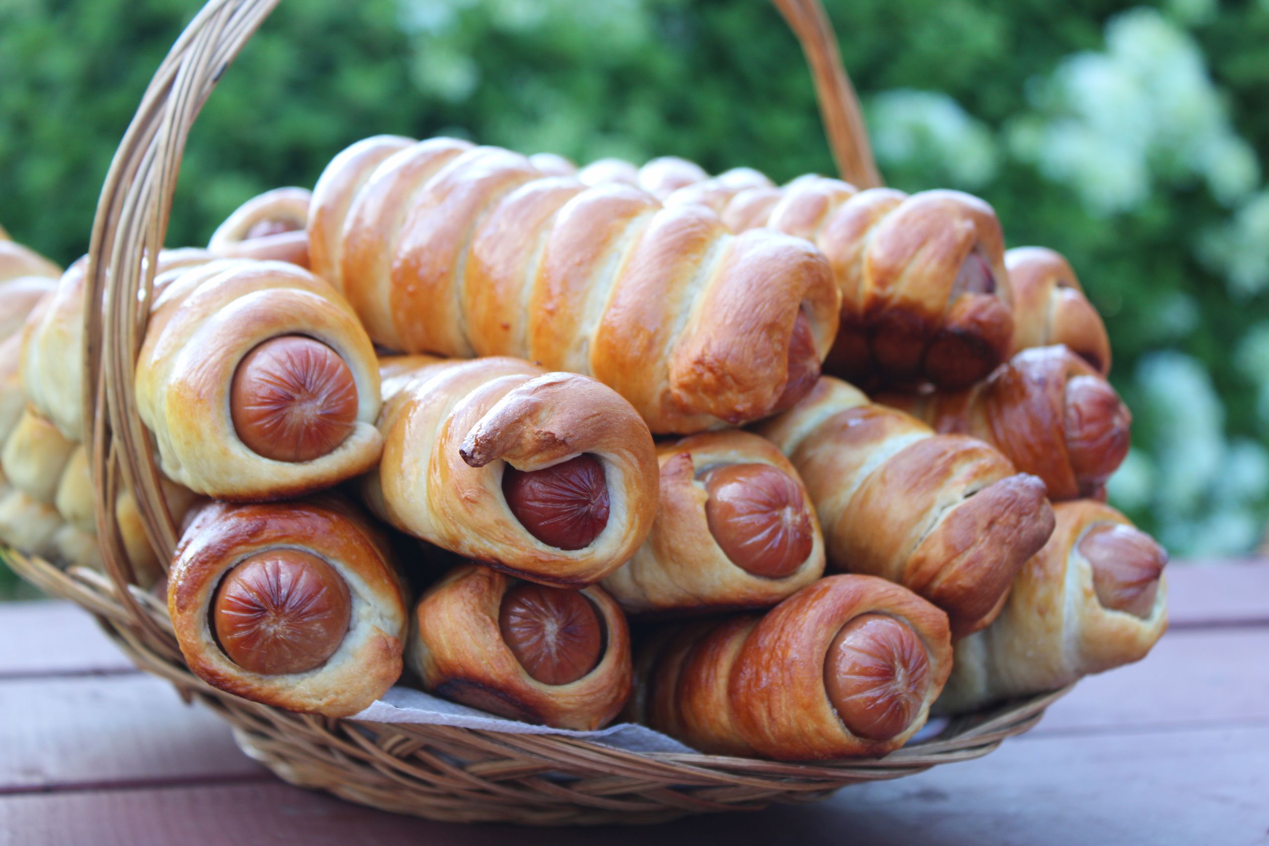 A close-up shot of freshly baked sausage rolls in a basket, outdoors.