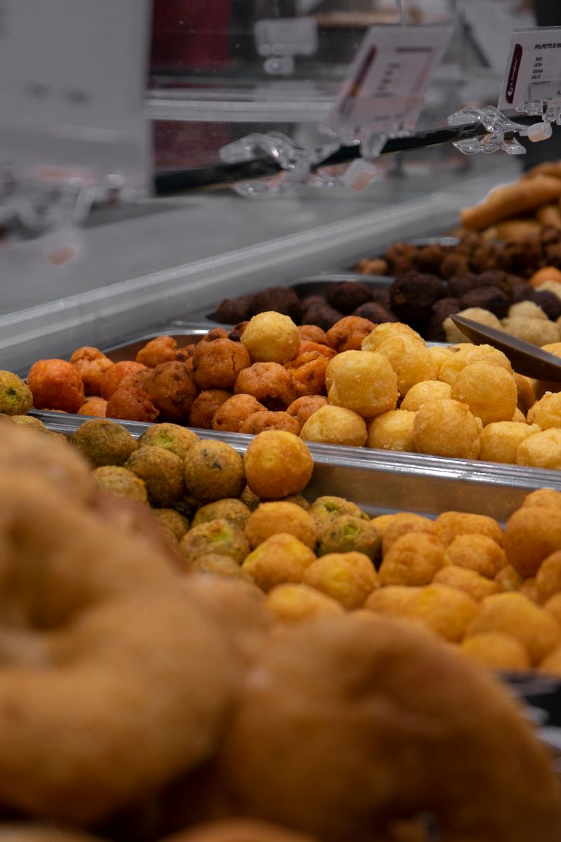 A close-up view of various colorful fried snack balls displayed in metal containers.