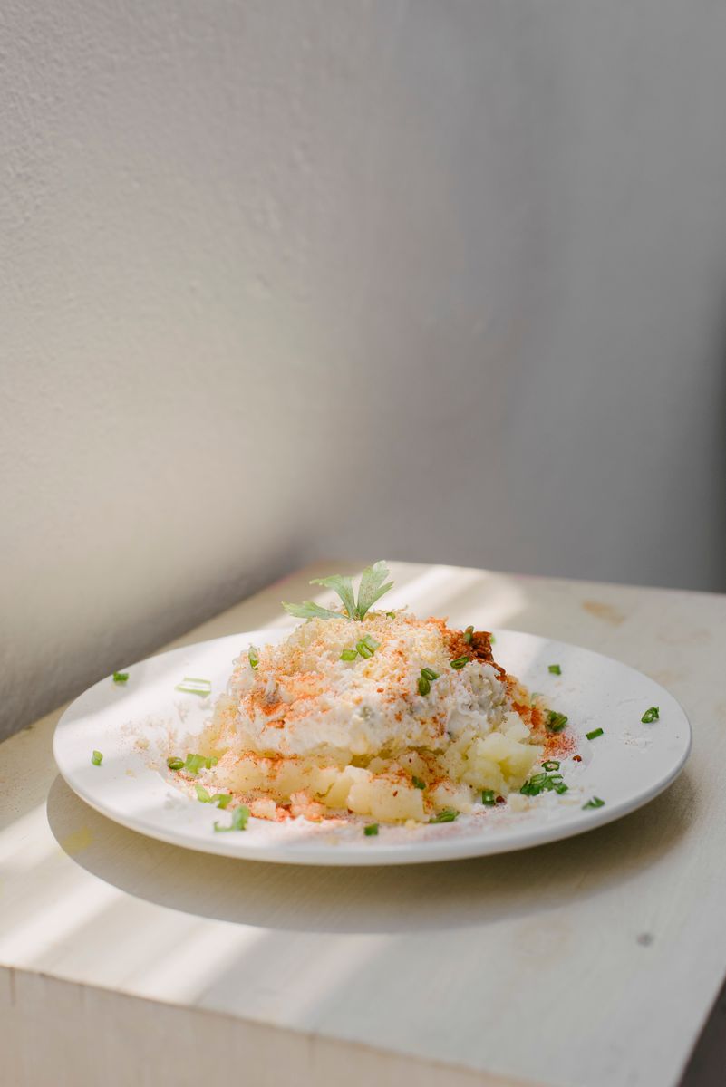 A creamy potato salad garnished with herbs on a white plate in soft natural light.
