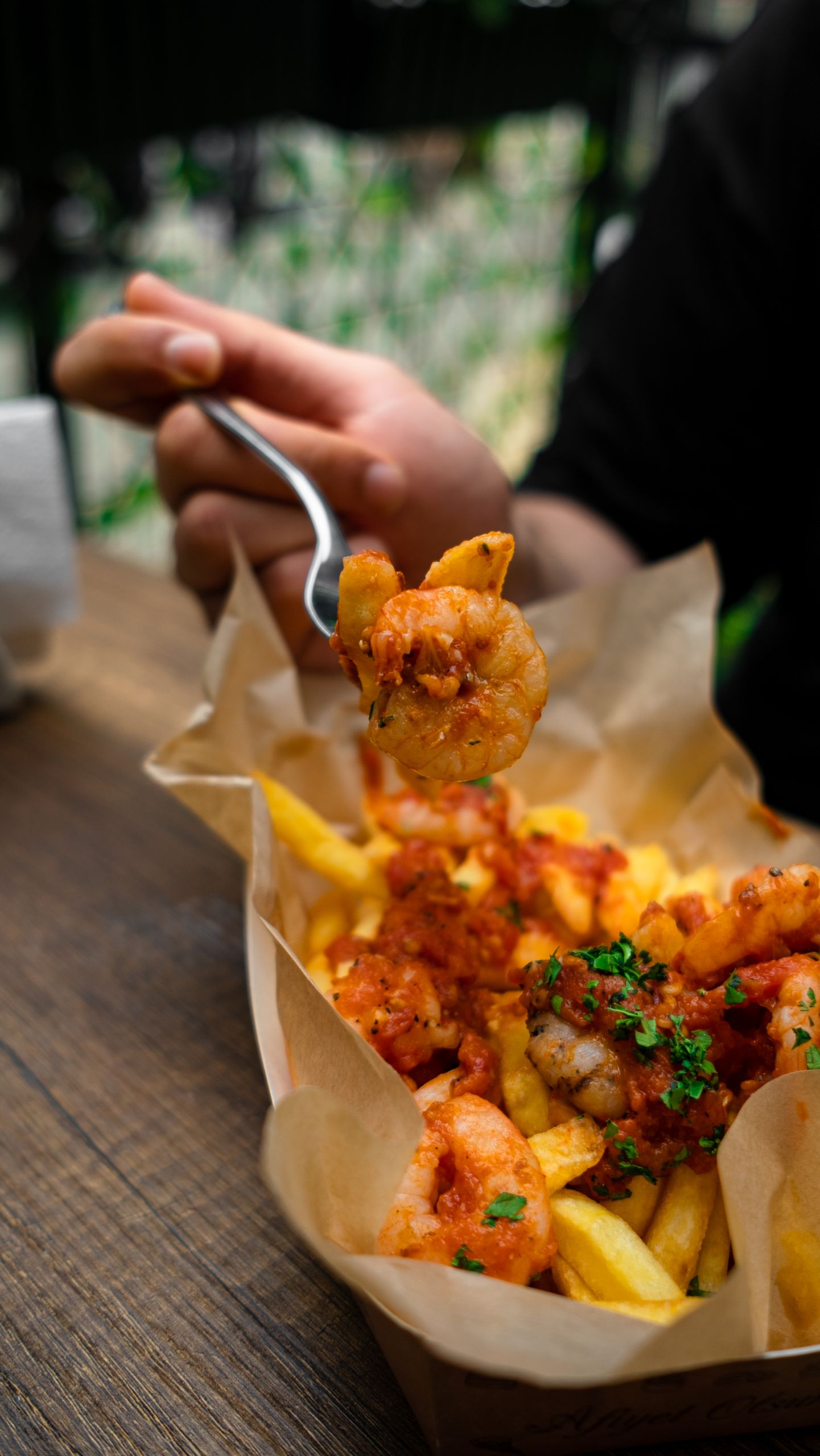 A hand holding a fork with shrimp over a basket of french fries, evoking a flavorful, indulgent meal.