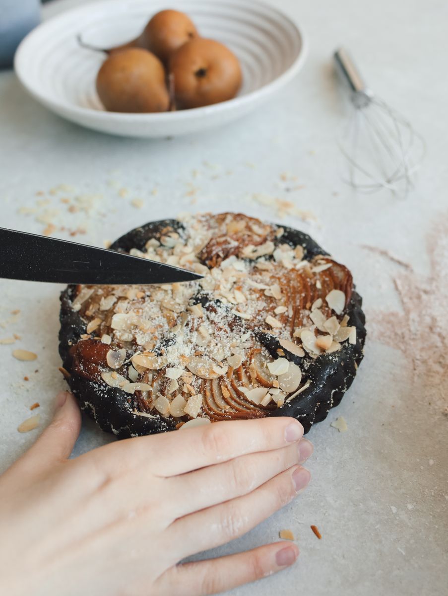 A person slices a beautifully homemade almond pear tart in a modern kitchen setting.
