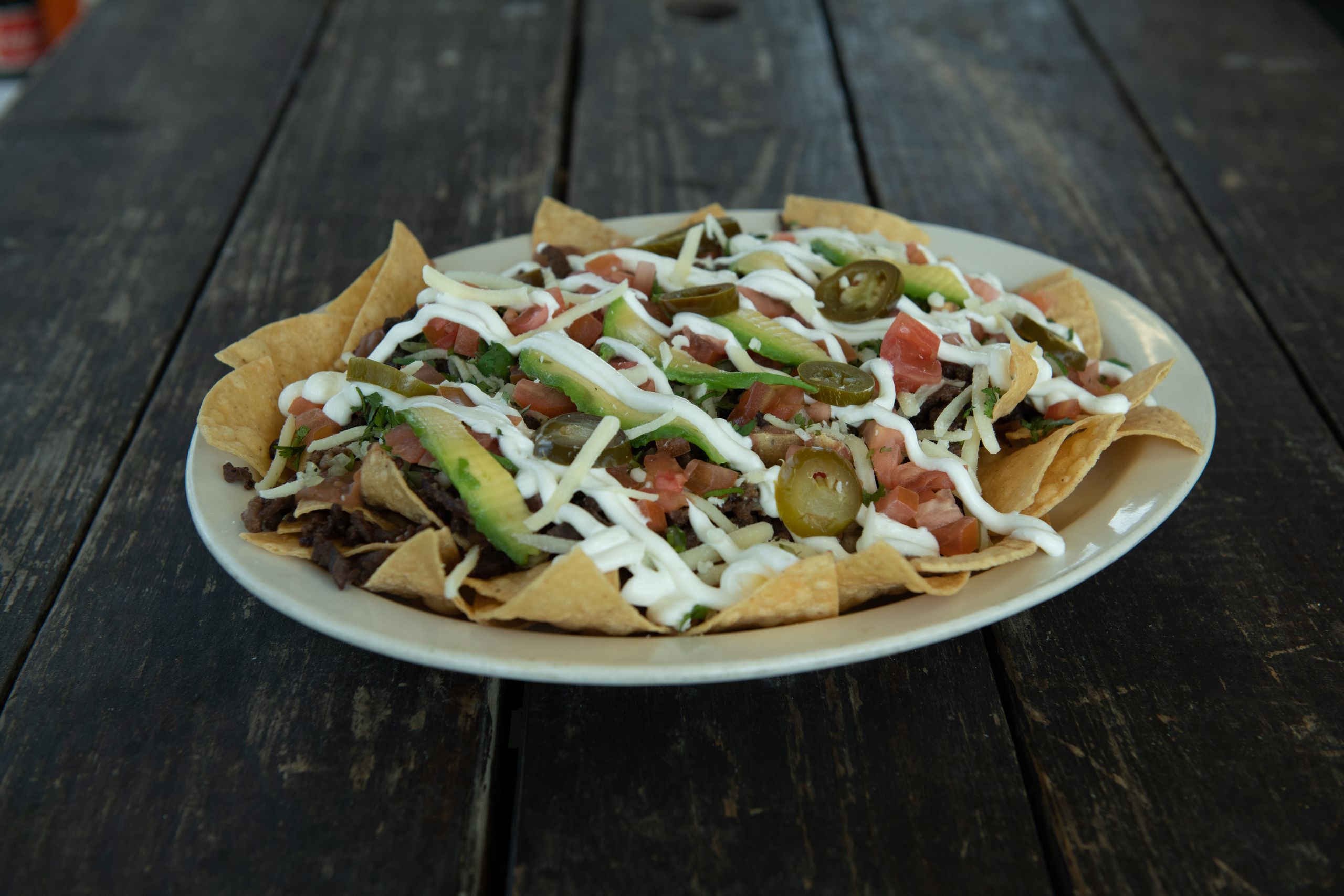 A plate of beef nachos topped with jalapenos, guacamole, and sour cream, perfect for a party or game night.