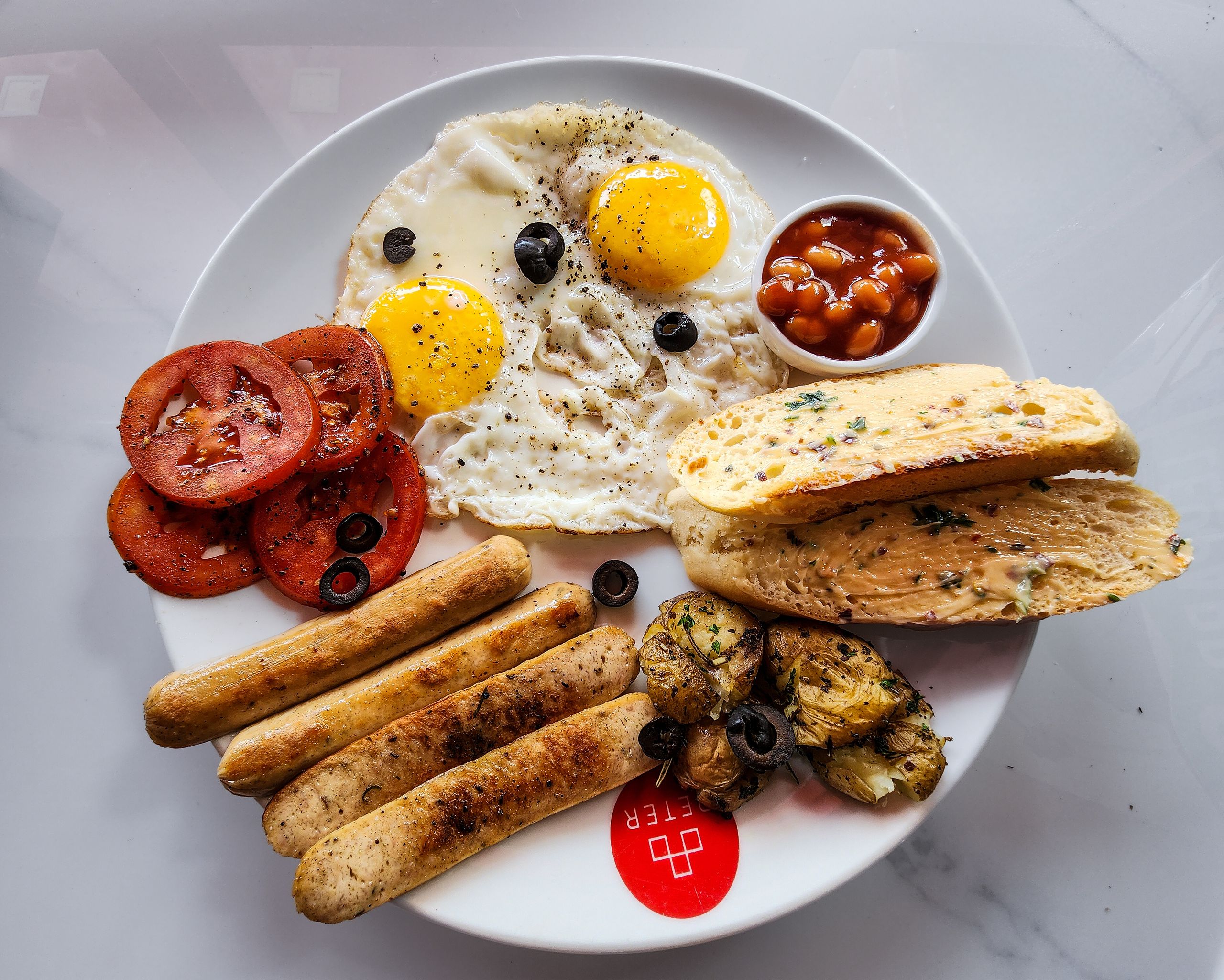 A top-down view of a classic English breakfast featuring fried eggs, sausage, and grilled tomatoes.
