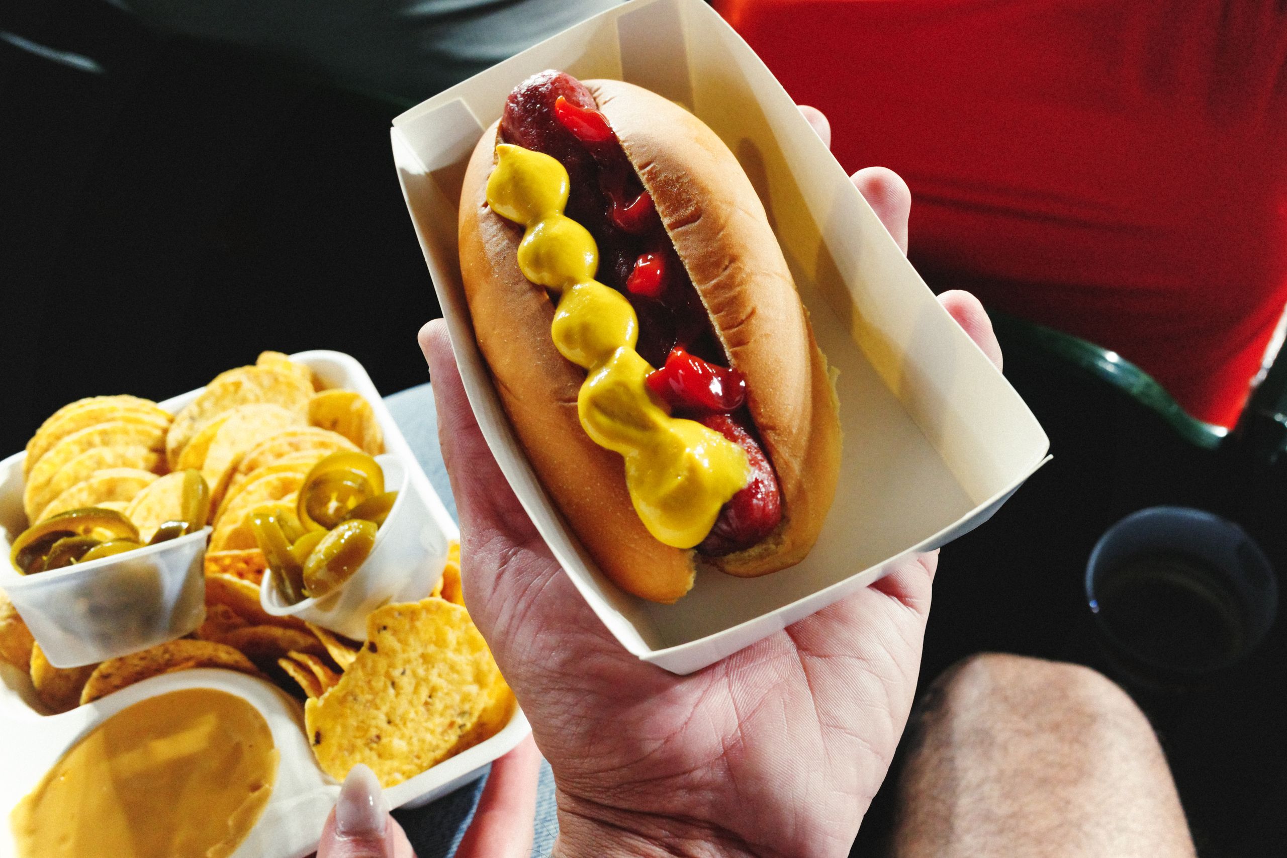 A traditional ballpark meal featuring a hot dog with mustard and ketchup and a side of nachos with cheese.