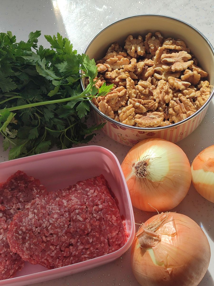 A vibrant composition with meat, walnuts, onions, and fresh herbs ready for cooking.