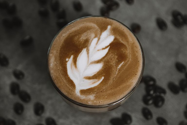 Aerial view of intricate latte art in a coffee cup surrounded by coffee beans.